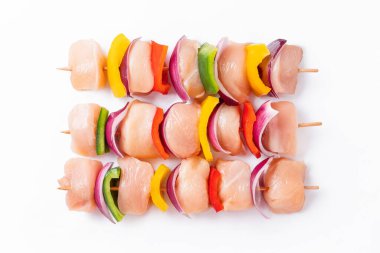 Uncooked mixed meat skewer with peppers.Raw chicken skewers with vegetables, peppers, onions, on a white background.Skewers with pieces of raw meat, red, yellow and green pepper.Top view.