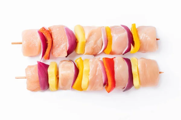 Raw pieces of chicken skewers with pepper onion and pineapple on a white background.Uncooked mixed meat skewer with peppers.Skewers with pieces of raw meat, red, yellow and green pepper.Top view.