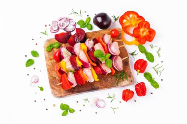 Skewers with pieces of raw meat, red, yellow and green pepper.Top view.Raw chicken leg meat skewers with vegetables,plums,peppers,onions, on a white background.Uncooked mixed meat skewer with peppers.