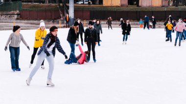 04.01.2022.Budapest.Soft,Selective focus.Children and adults are skating on a winter day at an outdoor skating rink. A friend helps a girl to stand up, who fell down while skating.Family winter sport.
