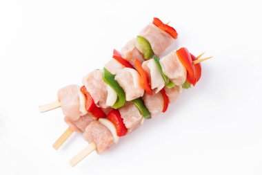 Top view.Uncooked mixed meat skewer with peppers.Raw turkey skewers with vegetables, peppers, onions on a white background.Skewers with pieces of raw meat, red, and green pepper, on white background.