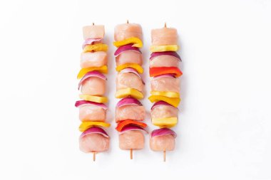 Top view.Skewers with pieces of raw meat, red, yellow and green pepper.Raw pieces of chicken skewers with pepper onion and pineapple on a white background.Uncooked mixed meat skewer with peppers.