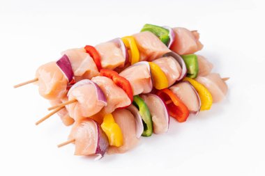 Skewers with pieces of raw meat, red, yellow and green pepper.Raw chicken skewers with vegetables, peppers, onions, on a white background.Uncooked mixed meat skewer with peppers.Top view.