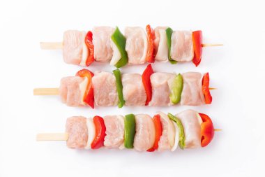 Top view.Uncooked mixed meat skewer with peppers.Raw turkey skewers with vegetables, peppers, onions on a white background.Skewers with pieces of raw meat, red, and green pepper, on white background.