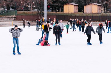 04.01.2022.Budapest.Soft,Selective focus.Children and adults are skating on a winter day at an outdoor skating rink. A friend helps a girl to stand up, who fell down while skating.Family winter sport.