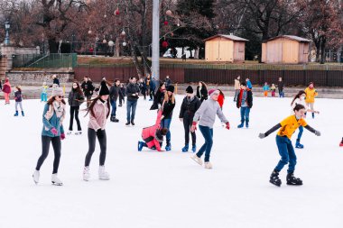04.01.2022.Budapest.Soft,Selective focus.Children and adults are skating on a winter day at an outdoor skating rink. A friend helps a girl to stand up, who fell down while skating.Family winter sport.