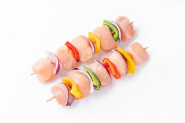Uncooked mixed meat skewer with peppers.Top view.Skewers with pieces of raw meat, red, yellow and green pepper.Raw chicken skewers with vegetables, peppers, onions, on a white background.
