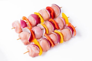 Skewers with pieces of raw meat, red, yellow and green pepper.Top view.Uncooked mixed meat skewer with peppers.Raw chicken leg meat skewers with vegetables, peppers, onions, on a white background.