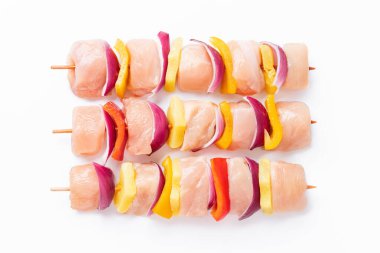 Skewers with pieces of raw meat, red, yellow and green pepper.Raw pieces of chicken skewers with pepper onion and pineapple on a white background.Uncooked mixed meat skewer with peppers.Top view.