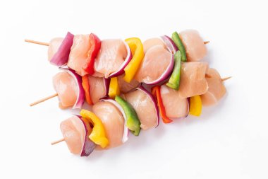 Uncooked mixed meat skewer with peppers.Raw chicken skewers with vegetables, peppers, onions, on a white background.Skewers with pieces of raw meat, red, yellow and green pepper.Top view.