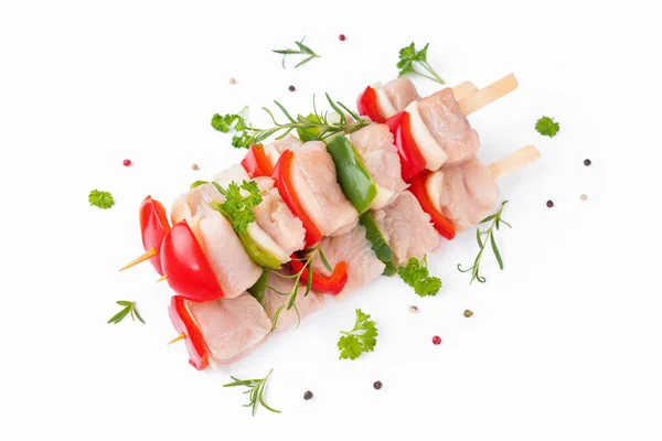 Skewers with pieces of raw meat, red, and green pepper, on white background.Uncooked mixed meat skewer with peppers.Raw turkey skewers with vegetables, peppers, onions on a white background.Top view.