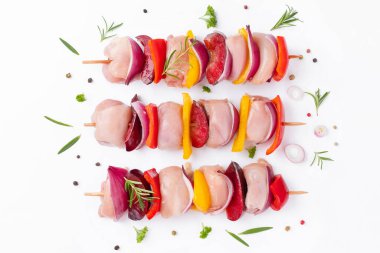 Uncooked mixed meat skewer with peppers.Raw chicken leg meat skewers with vegetables,plums,peppers,onions, on a white background.Skewers with pieces of raw meat, red, yellow and green pepper.Top view.