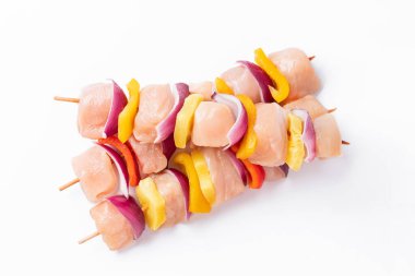 Skewers with pieces of raw meat, red, yellow and green pepper.Raw pieces of chicken skewers with pepper onion and pineapple on a white background.Uncooked mixed meat skewer with peppers.Top view.