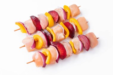 Uncooked mixed meat skewer with peppers.Raw chicken skewers with vegetables, peppers,plums,onions, on a white background.Skewers with pieces of raw meat, red, yellow and green pepper.Top view.