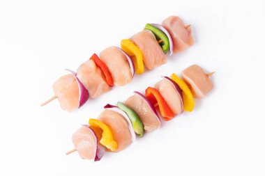 Skewers with pieces of raw meat, red, yellow and green pepper.Raw chicken skewers with vegetables, peppers, onions, on a white background.Uncooked mixed meat skewer with peppers.Top view.