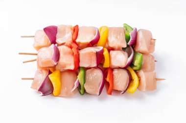 Raw chicken skewers with vegetables, peppers, onions, on a white background.Uncooked mixed meat skewer with peppers.Skewers with pieces of raw meat, red, yellow and green pepper.Top view.
