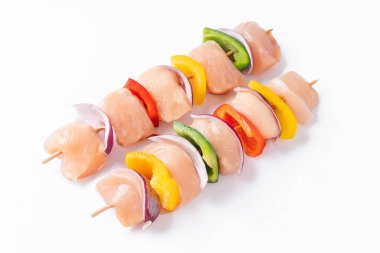 Uncooked mixed meat skewer with peppers.Top view.Skewers with pieces of raw meat, red, yellow and green pepper.Raw chicken skewers with vegetables, peppers, onions, on a white background.