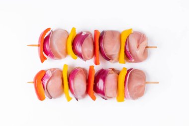 Uncooked mixed meat skewer with peppers.Raw chicken leg meat skewers with vegetables, peppers, onions, on a white background.Skewers with pieces of raw meat, red, yellow and green pepper.Top view.