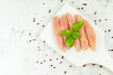 Tavuk göğsü filetoları. Kapatın. Çiğ tavuk eti. Taze bitkilerle dolu gri bir arka planda çiğ tavuk filetosu..