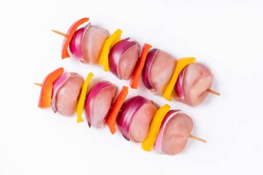 Skewers with pieces of raw meat, red, yellow and green pepper.Top view.Uncooked mixed meat skewer with peppers.Raw chicken leg meat skewers with vegetables, peppers, onions, on a white background.