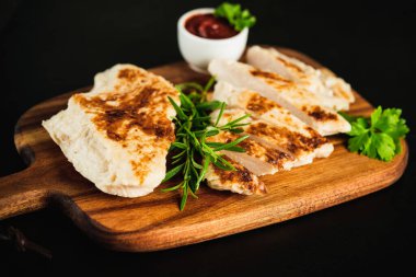 Yarı pişmiş, yarı pişmiş tavuk filetosu. Evde çabuk pişiyor. Hafif kızarmış tavuk filetosu, taze bitkilerle birlikte koyu bir arka planda..