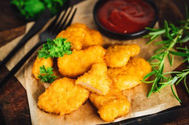 Yarı pişmiş tavuk nuggetları. Koyu bir arka planda taze bitkilerle birlikte tavuk filetosu. Fast food. Evde çabuk pişiyor. Köfteli tavuk filetosu. Hızlı pişirme. Salatalı tavuk nugget..