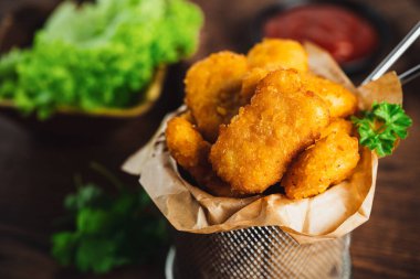 Yarı pişmiş tavuk nuggetları. Koyu bir arka planda taze bitkilerle birlikte tavuk filetosu. Fast food. Evde çabuk pişiyor. Köfteli tavuk filetosu. Hızlı pişirme. Salatalı tavuk nugget..