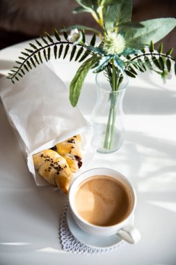 Güneşli sabahlarda kahvaltı: Kafenin iç kısımlarında kahve ve kruvasan, bitkiler ve buğdayla süslenmiş.