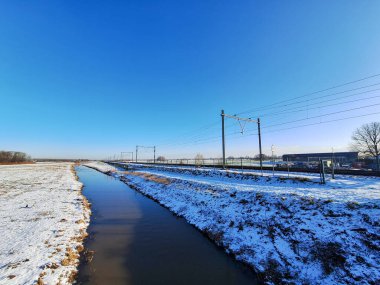 Hollanda 'daki demiryolu raylarının yakınındaki Zuidplaspold' un arta kalan turba bölgesinde kar bulunan donmuş çayırlar.