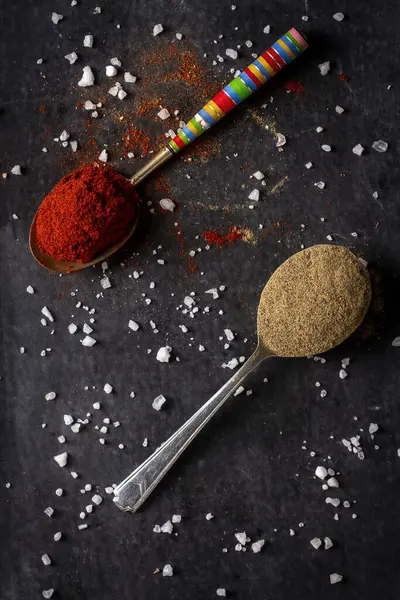 Old spoons with ground pepper and red paprika powder on black background. Flat lay. Top view. Food concept. Dark mood food photography.