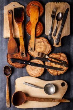 Old wooden cutting boards, tree trunk slices and kitchen utensils on black chalkboard background. Flat lay. Top view. Food concept. clipart