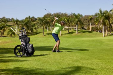Golf sahasında golf oynamaya hazır bir golfçü. Golf sopalı bir golfçü mükemmel atış için topa vuruyor..
