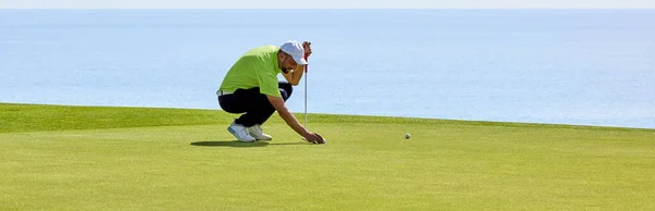 彼の手にパターで緑の上にゴルファー 緑のプレーヤーは フラグに向かってボールを目指す前に 穴からの斜面や距離を評価します — ストック写真