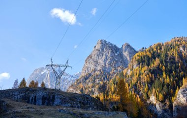 Dağlarda yüksek voltajlı elektrik pilonu. Arka planda Belluno Dolomites, Veneto, İtalya, Avrupa 'daki Marmolada kalabalığı, kayakçılar, yürüyüşçüler ve kar ayakkabıları için popüler bir durak..