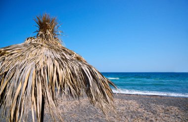 Paralia Karterados, sazdan şemsiyeli vahşi volkanik kum plajı. Yunan adaları, Santorini, Avrupa tatilleri.