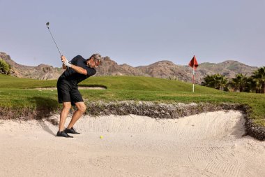 Bir golfçü golf sopasıyla topa vuruyor ve topu bayrağa olabildiğince yakın tutmaya çalışıyor..