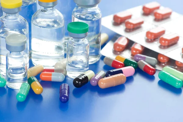 蓝色托盘上有许多不同颜色的药物胶囊和装有各种注射疫苗瓶的铝箔包 — 图库照片