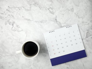 Calendar with coffee cup on marble texture background.