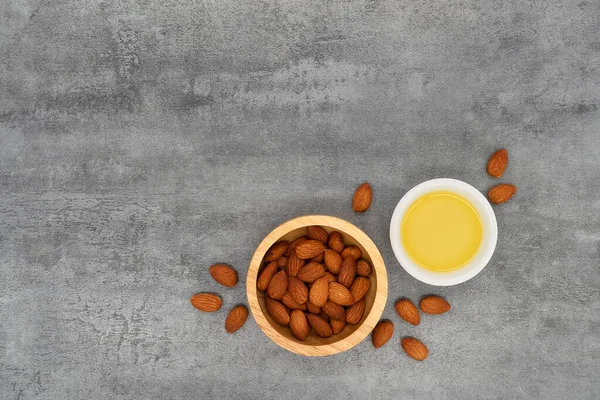 Almond oil in bowl and group of almond nuts on stone texture background. Almond oil with almond seeds. Top view.