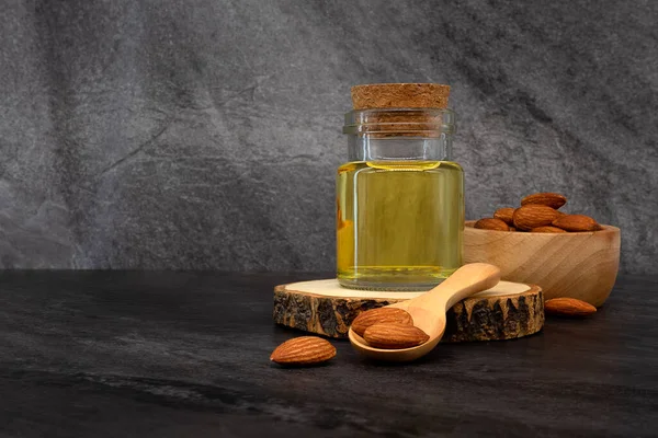 Almond oil in glass bottle and group of almond nuts on stone texture background. Almond oil with almond seeds.