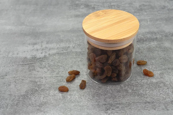 Raisins in glass jar on stone texture background. Dry raisins. Bulk raisins grains.