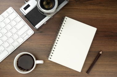 Ofis masasının üstünde klavye bilgisayarı, kitap ve eski kamerayla üst görüntü. İş ve finans kavramı. İş yeri. Boş fotokopi alanı olan düz bir yer. Ahşap doku.