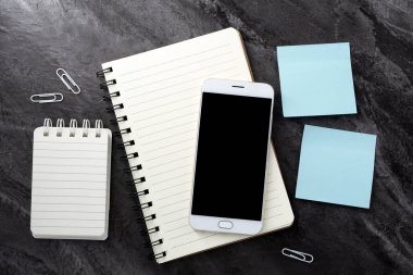 Boş ekran görüntülü cep telefonu ve siyah taş desenli özgeçmiş üzerine not defteri. Çalışma masası. Üst Manzara. Düz yatıyordu.