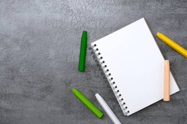 Defter ve renkli pastel boya kalemleri, taş dokusu arka planında. Çalışma masası alanı