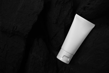 Siyah taşın üzerinde beyaz krema tüpü. Model için..