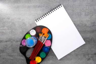Fırçalı suluboya palet ve taş dokusu üzerine kitap. Sanatçı çalışma alanı