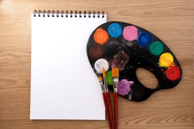 Fırçalı suluboya palet ve ahşap dokular üzerine kitap. Sanatçı çalışma alanı