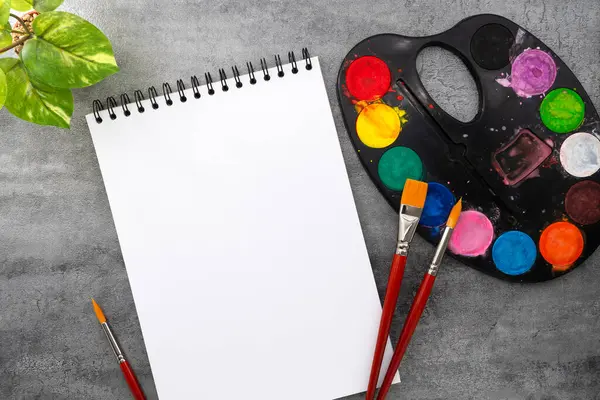 Fırçalı suluboya palet ve taş dokusu üzerine kitap. Sanatçı çalışma alanı
