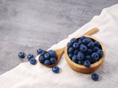 Ahşap kasede yaban mersini ve kaşık, taş desenli arka planda kumaş.