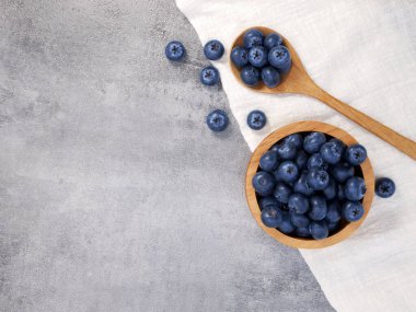 Ahşap kasede yaban mersini ve kaşık, taş desenli arka planda kumaş.